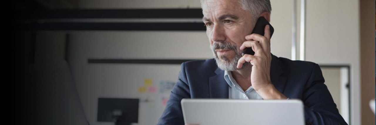 Man holding mobile phone looking at laptop